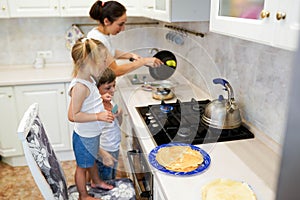 Family, children, hapiness and people concept. Happy family with children preparing pancakes in the kitchen. daughter helps