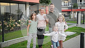 Family with children looking at camera standing on street outdoors. Couple and kids buying new home. Real estate owners