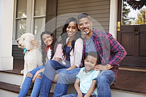 Family With Children And Pet Dog Sit On Steps Of Home