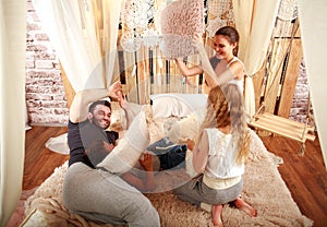 Family with children playing with pillows at home on bed