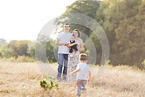 Family with children walking outdoors in summer field at sunset. Father, mother and two children sons having fun in