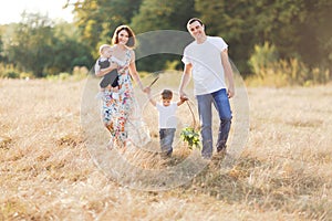 Family with children walking outdoors in summer field at sunset. Father, mother and two children sons having fun in