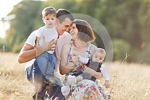 Family with children walking outdoors in summer field at sunset. Father, mother and two children sons having fun in