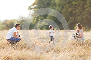 Family with children walking outdoors in summer field at sunset. Father, mother and two children sons having fun in