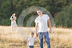 Family with children walking outdoors in summer field at sunset. Father, mother and two children sons having fun in