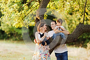 Family with children walking outdoors in summer field at sunset. Father, mother and two children sons having fun in