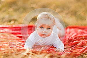 Family with children walking outdoors in summer field at sunset. Little baby boy lying on red plaid having fun in summer