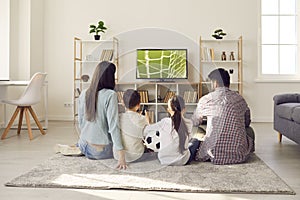 Family with children watching football match together at home cheering for their favorite team.