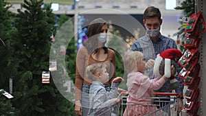 The family chooses the scenery in the supermarket. A happy family in medical masks in the store buys Christmas