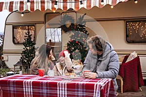 Family Christmas in camper: young mum, dad and kid drink hot cocoa outside Rv car decorated for Xmas