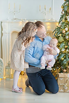 Family on Christmas eve at fireplace. Kids opening Xmas presents. Children under Christmas tree with gift boxes. Decorated living