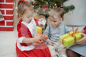 Family on Christmas eve at fireplace. Mother and little kids opening Xmas presents. Children with gift boxes. Living