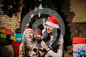 Family on Christmas eve. Mother and daughter and dog with Xmas presents. Family with gift boxes. Living room with decorated tree.