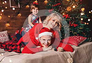 Family in Christmas Santa hats lying on bed. Mother, father and baby having fun in living room decorated by Christmas tree