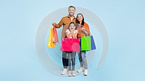 Family with colorful shopping bags standing together over blue backdrop