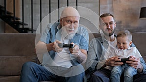 Family competes in games on console, have fun together. Happy family old grandpa's son and grandson are playing video