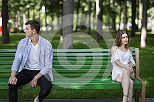 Family conflict. Young husband and wife sitting apart from each other on bench at park