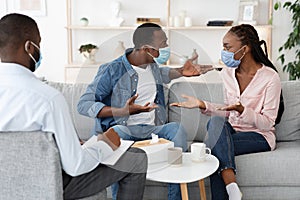 Family Conflicts. Black couple in medical masks arguing at at counselors office