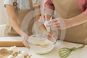 Family cooking. Maure lady adding egg to flour while little girl helping her in kitchen, closeup