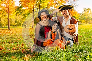 Family in costumes sit on grass with pumpkin