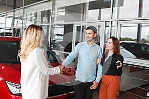 Family couple at car dealership. Husband shakes hands with a car dealer after a successful deal
