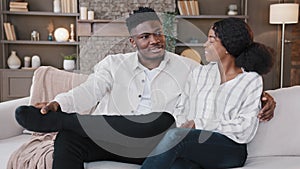 Family couple married spouses African man and biracial woman talking laughing sitting on sofa together in living room in