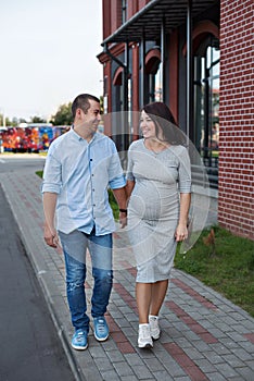 Family couple men and a young pregnant woman walking holding hands and laughing along the city windows