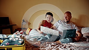 Family couple planning trip laying in bed. Using laptop and map discussing detail about destination excited. Woman