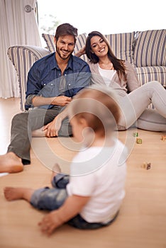 Family, couple and smile in lounge with toddler for growth, development and bonding on floor. Parents, caregivers and