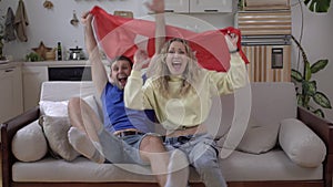 Family couple of sports fans at home with the flag of Turkey. Football fans of the Turkish national team are watching TV