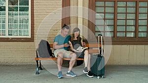 Family couple is waiting for train with phone and book. Technology vs tradition