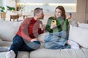 Family couple young man woman buying online in smartphone sitting on couch at home.