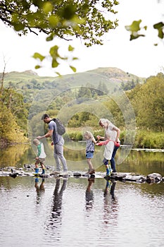 Family Crossing River Whilst Hiking In UK Lake District