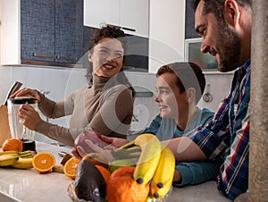 Family cutting fresh fruits and preparing juice in the kitchen for breakfast