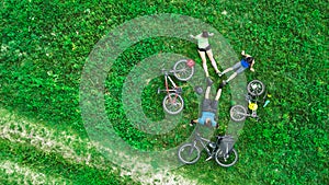 Family cycling on bikes aerial drone view from above, happy active parents with child have fun and relax on grass with bicycles