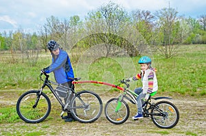 Family cycling, father teaches child to ride bicycle with bike tow bar, family sport and activity with kid outdoors