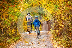 Family cycling in golden autumn park, active father and kids ride bikes, family sport and fitness with children