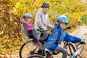 Family cycling in golden autumn park, active father and kids ride bikes, family sport and fitness with children