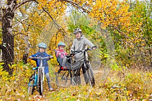 Family cycling in golden autumn park, active father and kids ride bikes, family sport and fitness with children