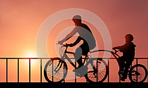 Family Cycling Together at Sunset time. Father and son silhouette Biking in front of beautiful sunset background