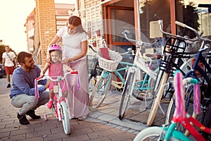 Family with daughter having fun outdoor shopping new bicycle and helmets