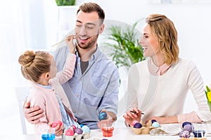 Family and daughter having fun while painting eggs