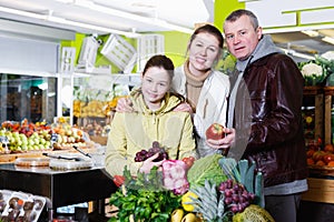 Family with daughter near full grocery cart in fruit store