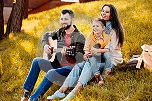 Family with daughter relaxing on a grassy hill while father playing
