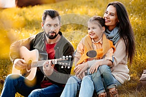 Family with daughter relaxing on a grassy hill while father playing