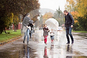 Family with daughters under the umbrellas, running. Rainy day.