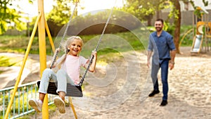 Family day. Happy girl swinging on swings having fun with father on playground, panorama, selective focus on schoolgirl