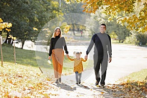Family day. Happy young mom and dad hold their little child daughter hands walk, have fun outdoor at autumn park, enjoy