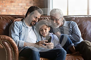 Retired grandpa young father preteen boy relax indoors use smartphone