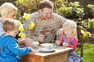 Family Decorating Easter Eggs On Table Outdoors